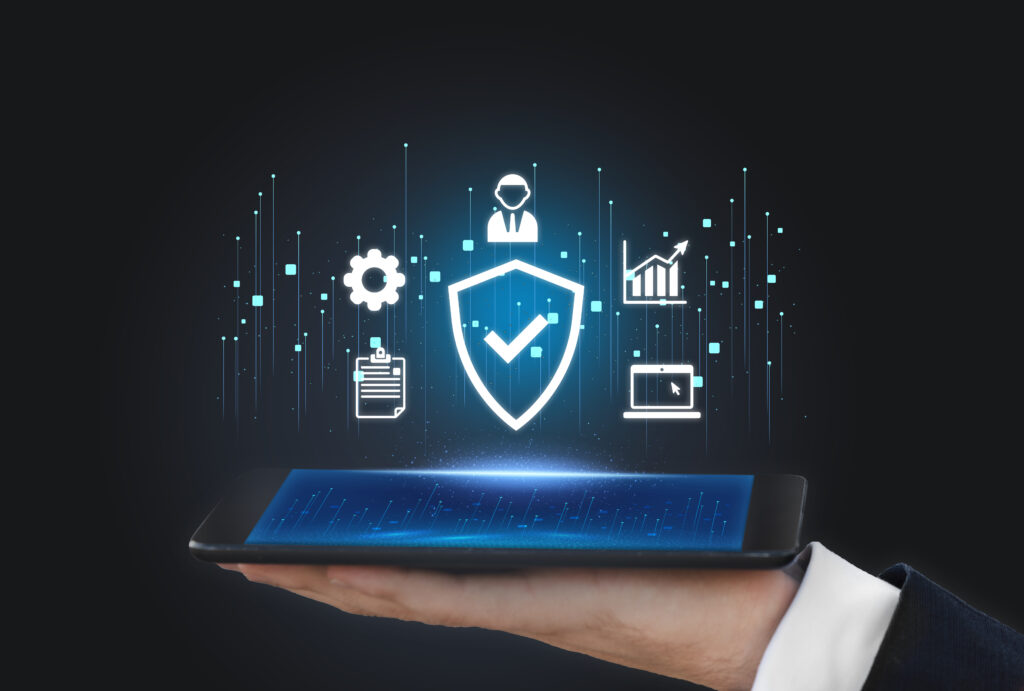 An image featuring a glowing digital shield with a checkmark, symbolizing data protection and security verification. The shield is surrounded by floating tech icons representing cloud systems, data analytics, and user management, hovering over a modern smartphone held in a professional’s hand. This visual represents the seamless integration of compliance automation software to manage frameworks like SOC 2, ISO 27001, and DPDP in a digital-first enterprise environment.