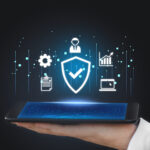An image featuring a glowing digital shield with a checkmark, symbolizing data protection and security verification. The shield is surrounded by floating tech icons representing cloud systems, data analytics, and user management, hovering over a modern smartphone held in a professional’s hand. This visual represents the seamless integration of compliance automation software to manage frameworks like SOC 2, ISO 27001, and DPDP in a digital-first enterprise environment.